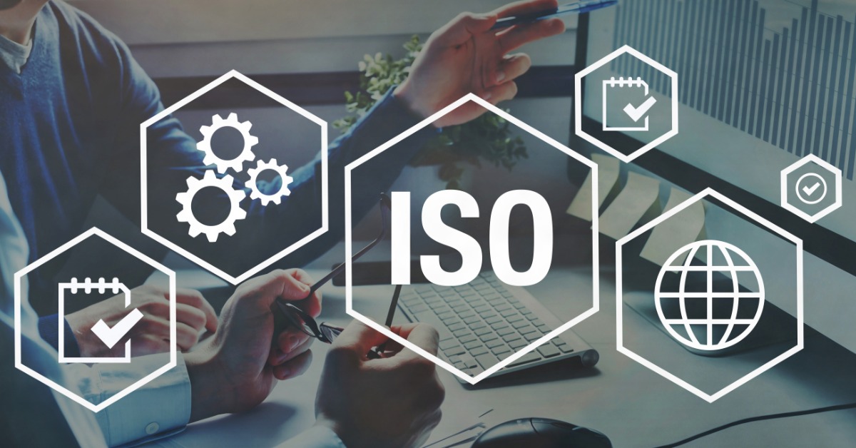 A close-up of two people sitting at a desk looking at a computer monitor with graphic icons overlaid that read "ISO."